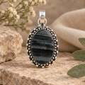 Medium oval black tourmaline pendant with a silver-tone beaded setting on a warm neutral display.