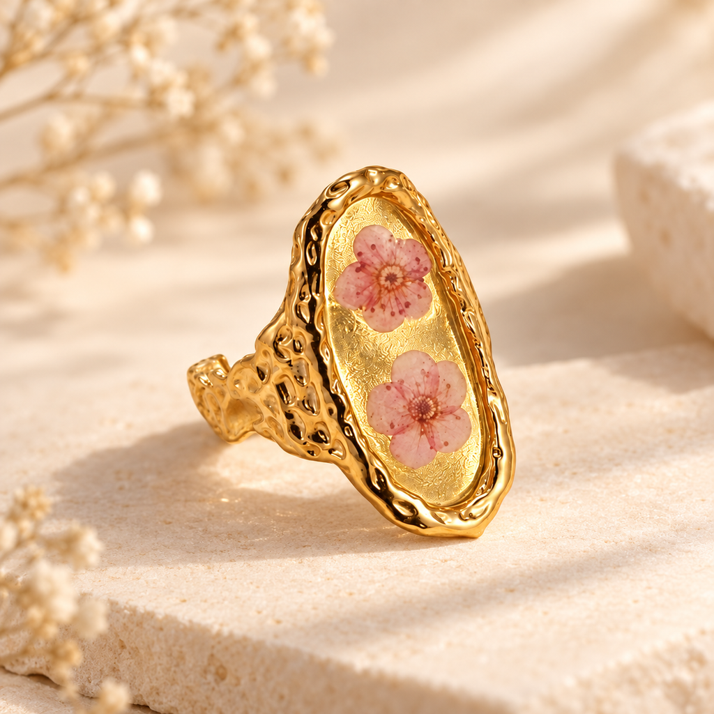Blushing Blossom Renewal Ring with two pink pressed blossoms in a gold-tone setting on a warm botanical background