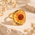 Golden Daisy Vitality Ring with a warm orange pressed daisy in an organic gold-tone setting on a warm botanical background