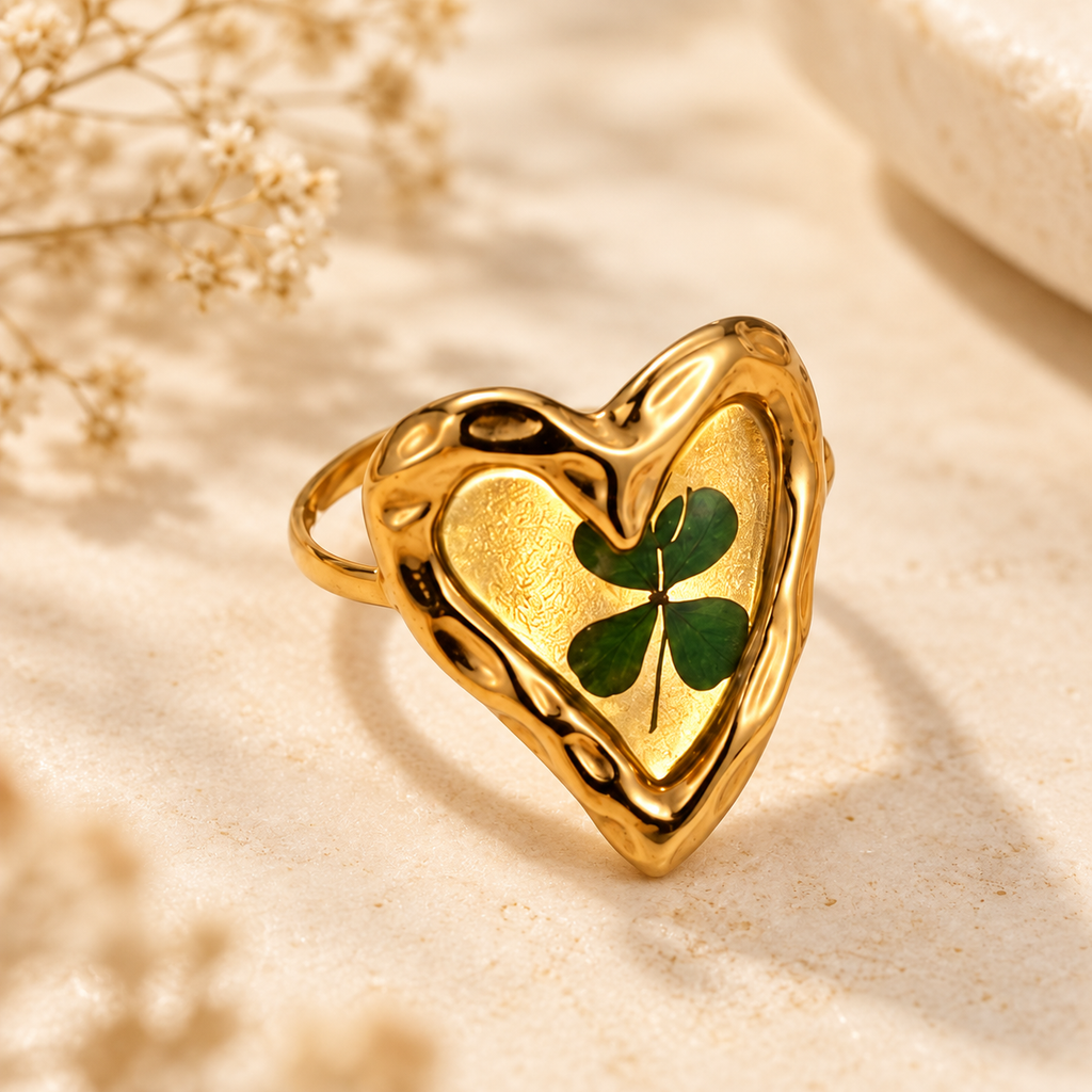 Lucky Roots Clover Heart Ring with a green four-leaf clover in an organic gold-tone heart setting on a warm botanical background