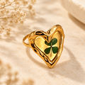 Lucky Roots Clover Heart Ring with a green four-leaf clover in an organic gold-tone heart setting on a warm botanical background