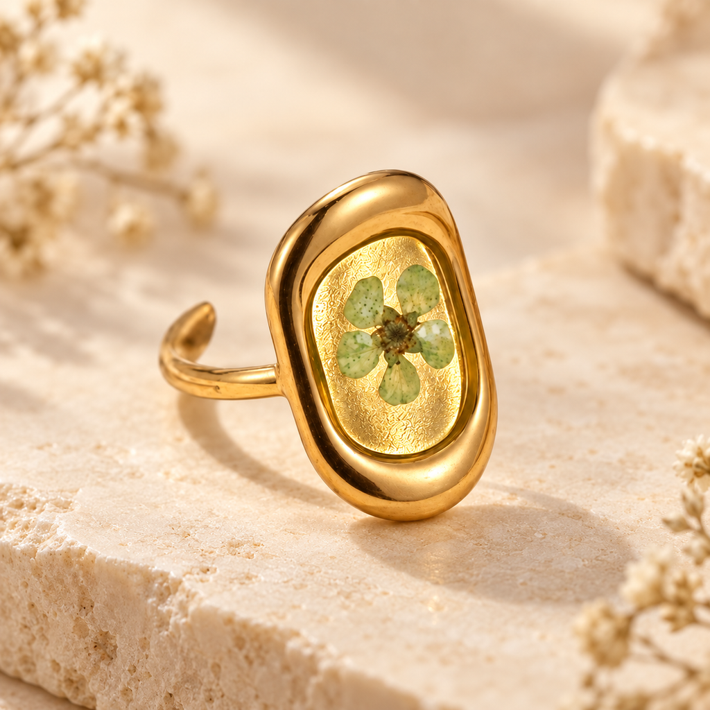 Meadow Green Bloom Ring with a pale green pressed flower in a smooth gold-tone oval setting on a warm botanical background