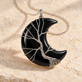 Black Obsidian crescent moon necklace wrapped with a silver-tone Tree of Life on a warm cream background.