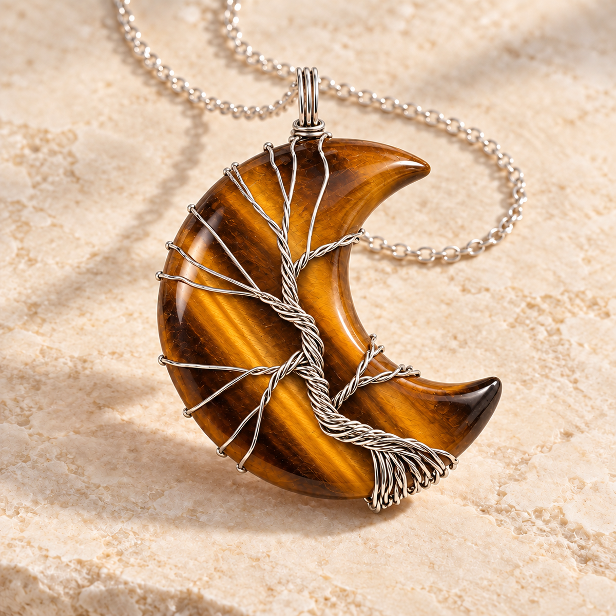 Tiger's Eye crescent moon necklace wrapped with a silver-tone Tree of Life on a warm cream background.