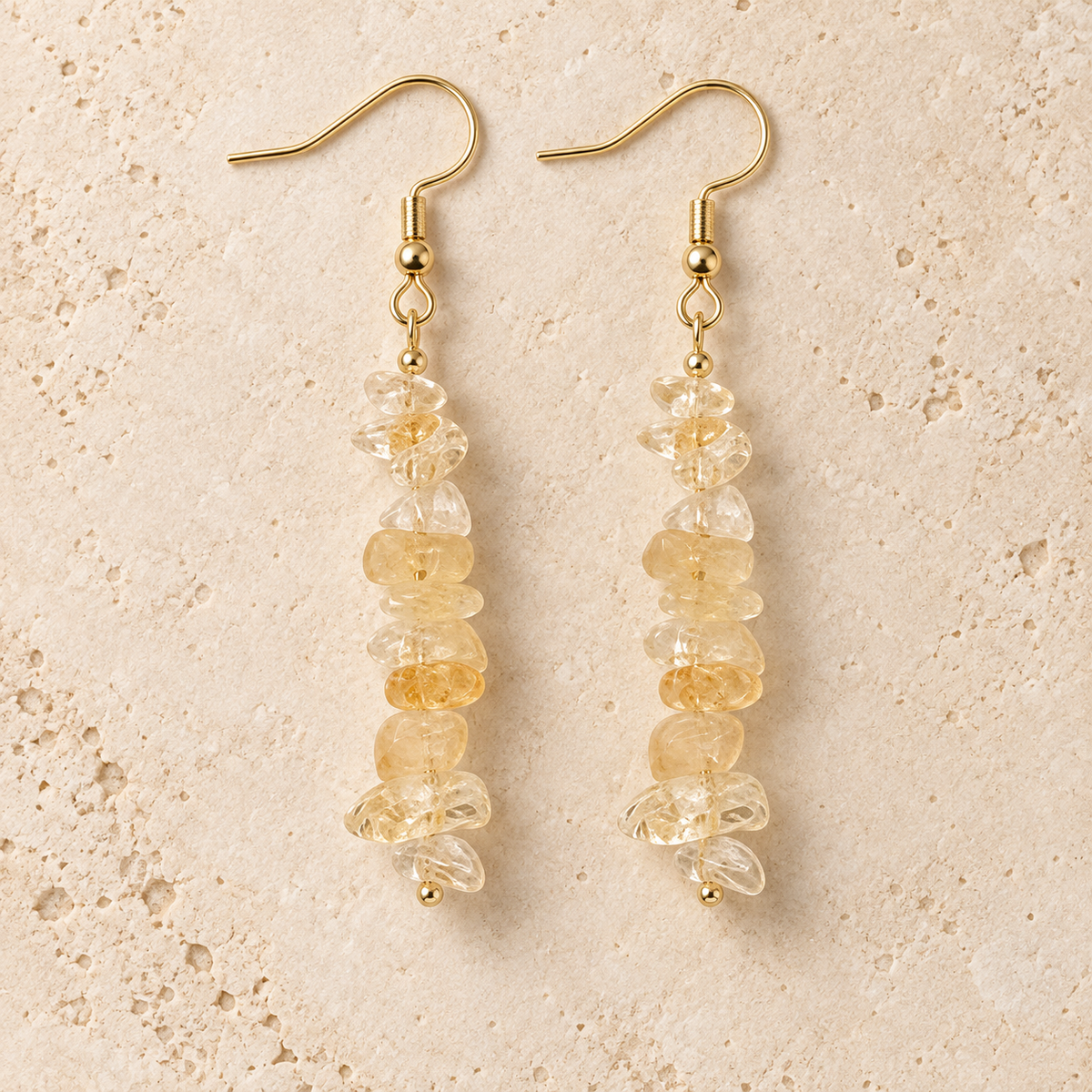 Citrine stone chip drop earrings with gold-tone hooks on a warm cream background.