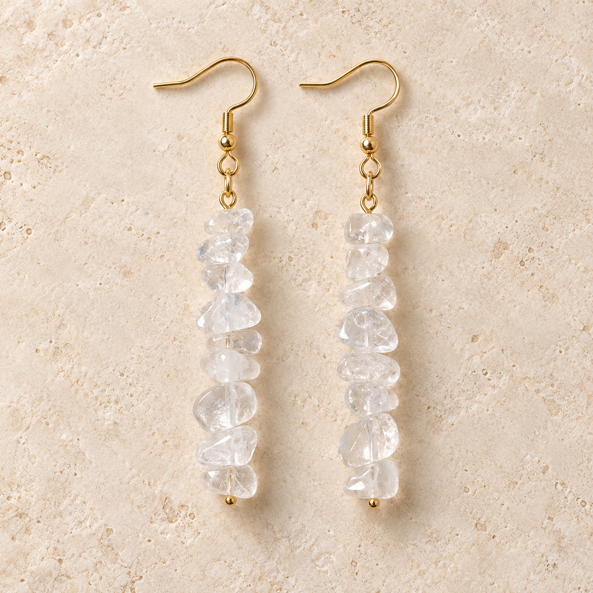 Clear Quartz stone chip drop earrings with gold-tone hooks on a warm cream background.