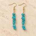 Turquoise stone chip drop earrings with gold-tone hooks on a warm cream background.