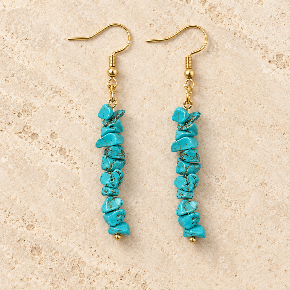 Turquoise stone chip drop earrings with gold-tone hooks on a warm cream background.