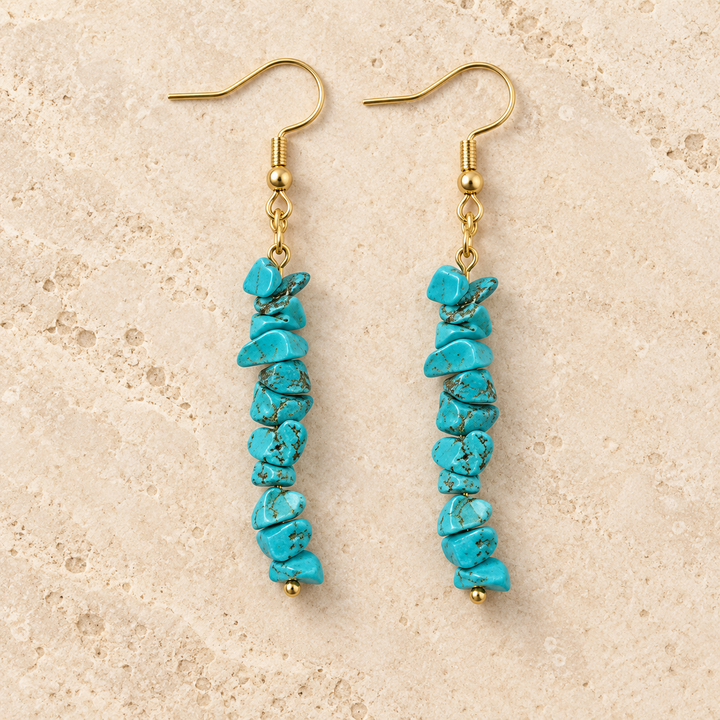 Turquoise stone chip drop earrings with gold-tone hooks on a warm cream background.