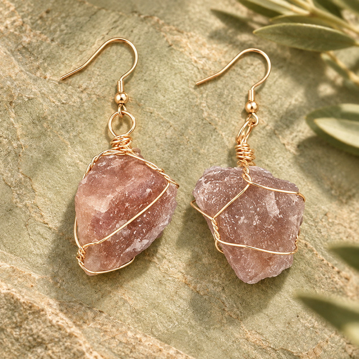Pair of muted mauve-brown rough stone earrings with gold-tone wire wrapping on a warm stone surface.