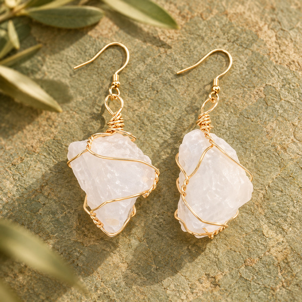 Pair of milky translucent white rough stone earrings with gold-tone wire wrapping on a warm stone surface.