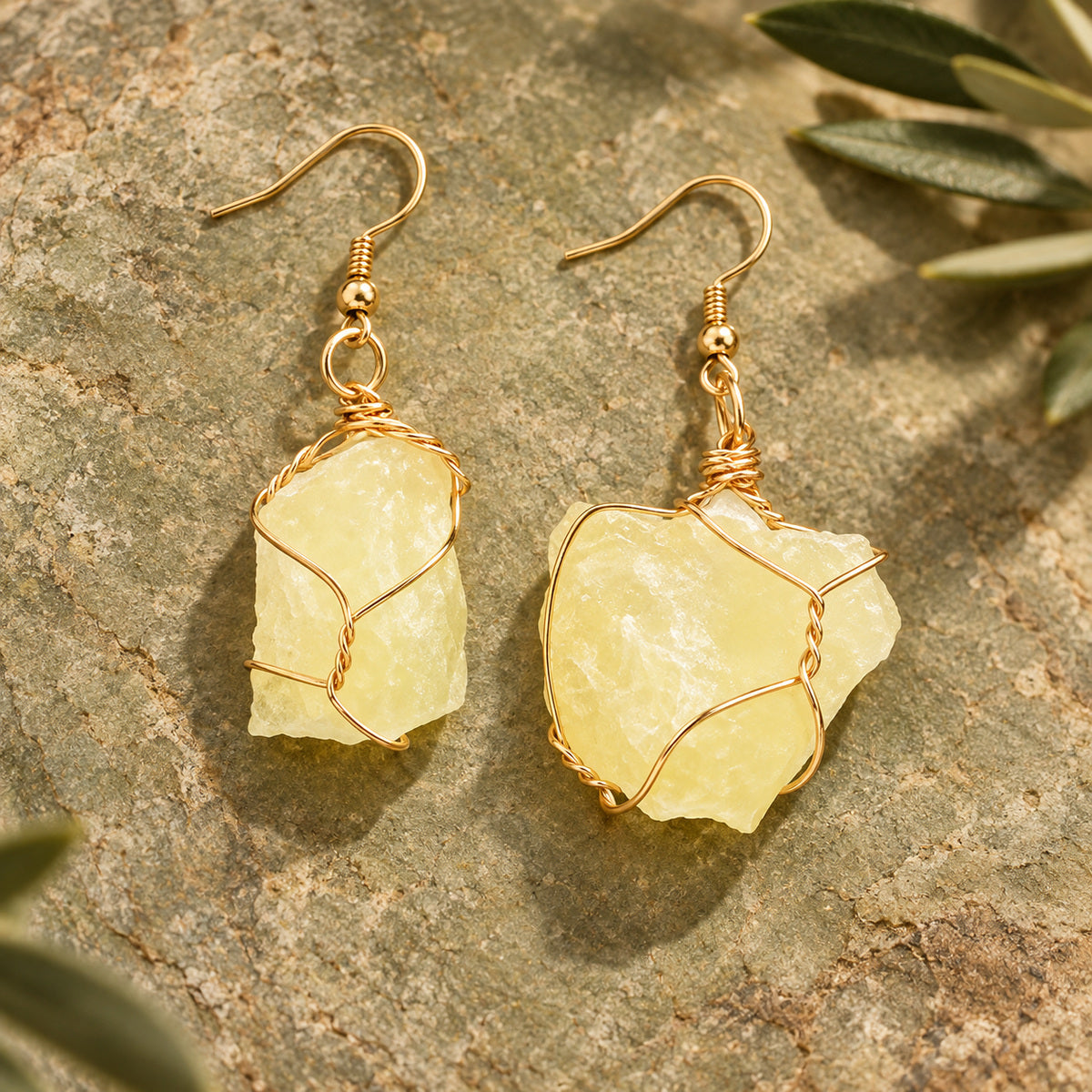 Pair of pale lemon yellow rough stone earrings with gold-tone wire wrapping on a warm stone surface.