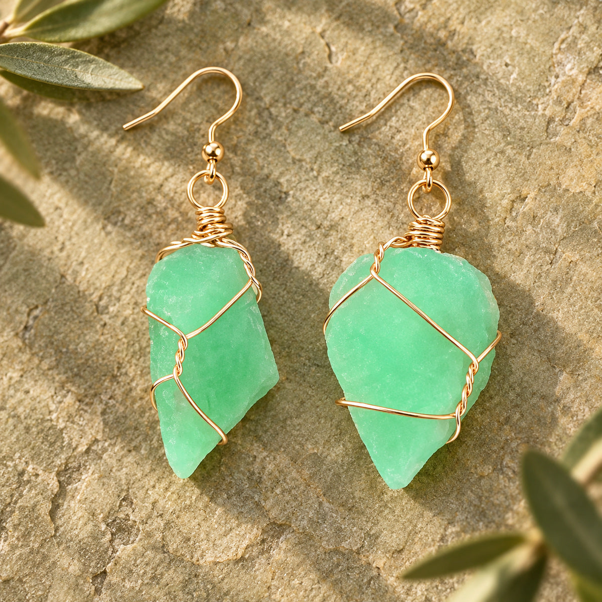 Pair of mint green rough stone earrings with gold-tone wire wrapping on a warm stone surface.