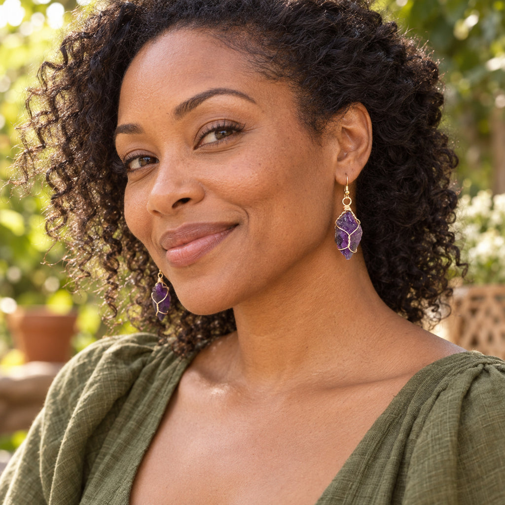 Model wearing deep purple rough stone earrings with gold-tone wire wrapping.