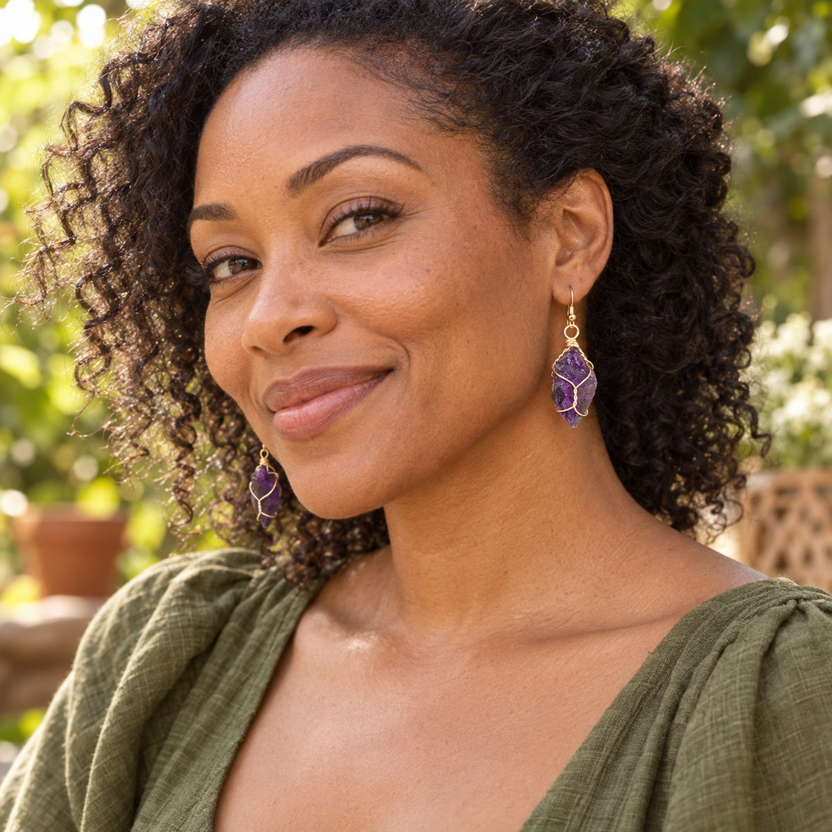 Model wearing deep purple rough stone earrings with gold-tone wire wrapping.