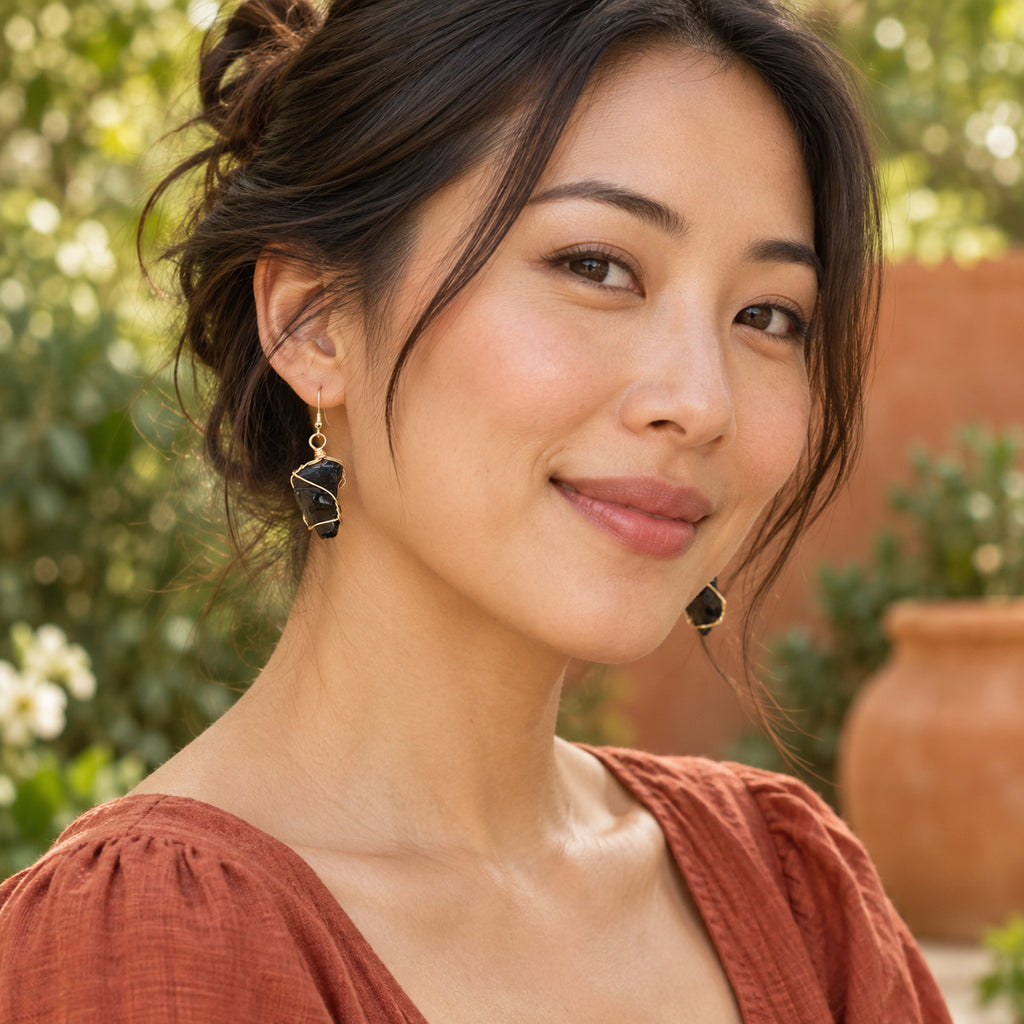 Model wearing glossy black rough stone earrings with gold-tone wire wrapping.