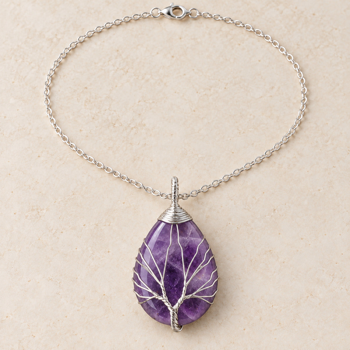 Amethyst teardrop Tree of Life necklace on a warm cream background.
