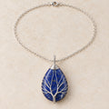 Lapis Lazuli teardrop Tree of Life necklace on a warm cream background.