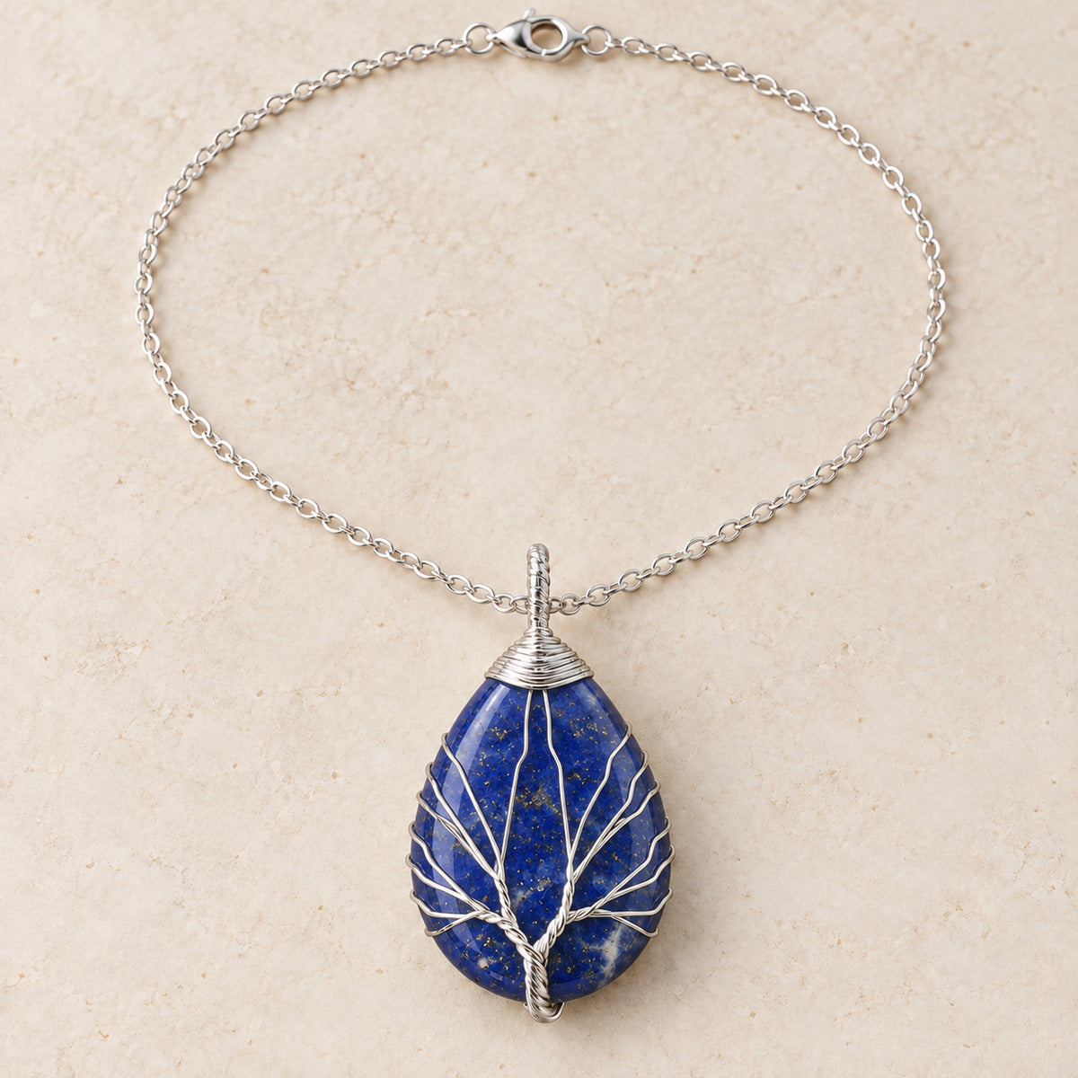 Lapis Lazuli teardrop Tree of Life necklace on a warm cream background.