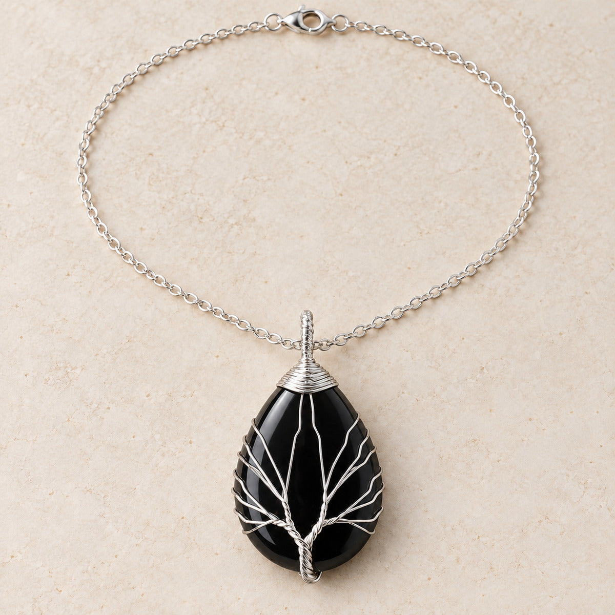 Obsidian teardrop Tree of Life necklace on a warm cream background.