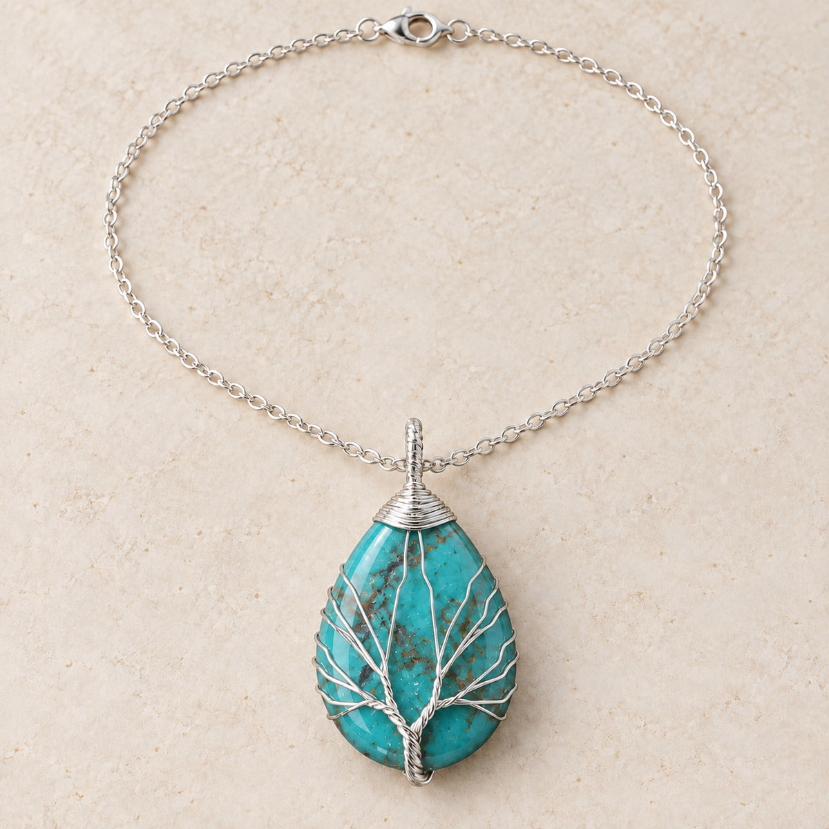Turquoise teardrop Tree of Life necklace on a warm cream background.